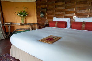 Bedroom with wooden panel headboard, large bed with white linens and red pillows, wooden furniture.