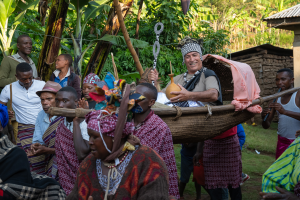 People dressed in traditional attire carrying a man in a woven basket during a cultural event outdoors.
