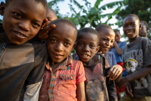 Group of young boys outdoors smiling with greenery and sky in the background.