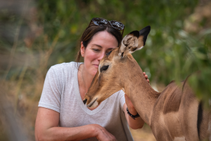 Woman in a white shirt gently touching a brown antelope with greenery in the background