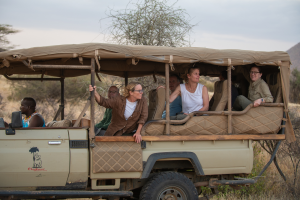 Open safari vehicle with passengers on a dry bushy landscape, Elephant Bedroom Camp logo visible.