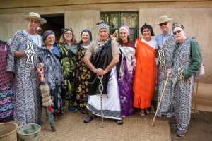 Group of people in traditional patterned clothing posing outdoors with woven baskets and staffs.