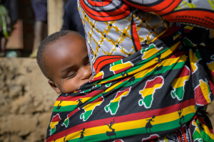 Sleeping child carried on adult's back in a vibrant cloth with map and human figure patterns