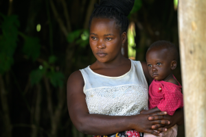 Woman in white sleeveless top holding a child in a pink outfit against a dark background
