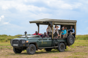 Safari vehicle with passengers on grassy terrain under a cloudy sky at Tangulia Mara camp