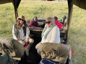 Four people seated in an open safari vehicle in a grassy savannah during a guided tour.