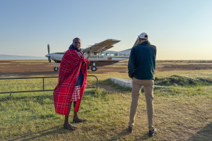 Two men standing near a Safarilink aircraft on grassy ground under a clear sky.
