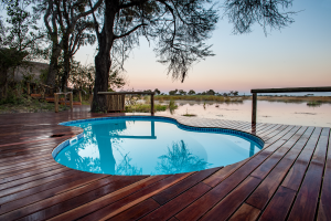 Small irregular pool with wooden deck near trees and calm water at sunset or sunrise.