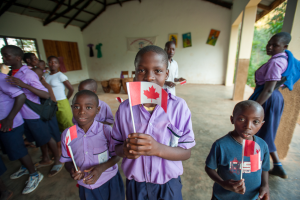 Children in purple uniforms holding small Canadian flags inside a building with drums and paintings.