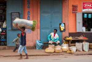 Street vendor selling grains and vegetables in front of a building with blue doors and orange wall.
