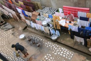 Outdoor area with two people ironing and sweeping surrounded by hanging clothes and cooking pots.