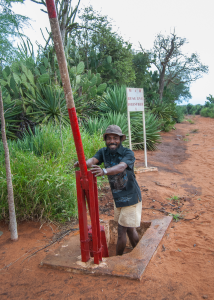 Man standing in a concrete well holding a red pump handle near a forest reserve sign.